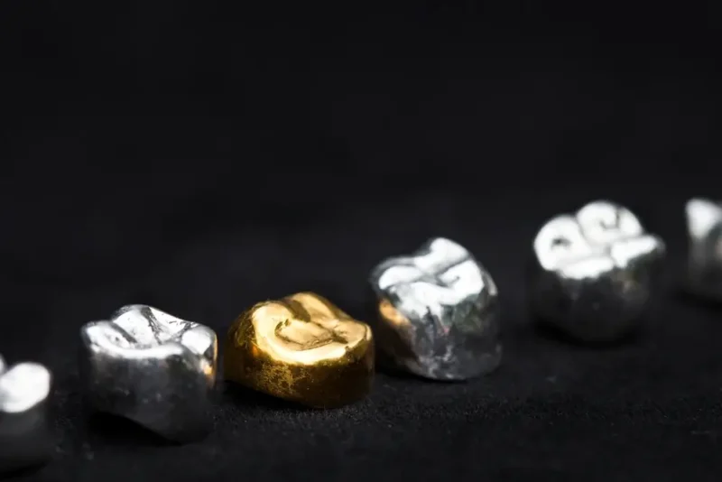 A prominent Gold Dental Crown placed in a row of silver metal crowns against a black background.